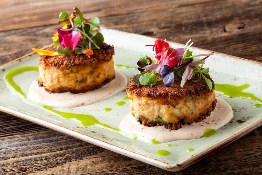 2 crab cakes on a plate decorate with flowers at Bluewater Boathouse Coronado