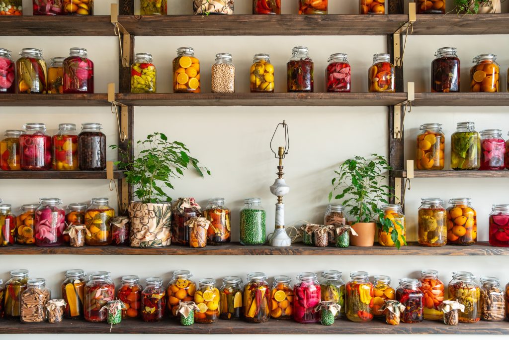 Wall with glass jars of colorful preserved vegetables on shelves