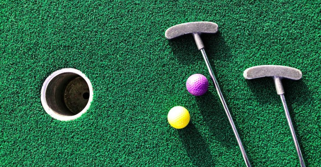 Green astroturf grass with two putt putt clubs and yellow and purple golf balls. San Diego Mini Golf.