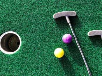 Green astroturf grass with two putt putt clubs and yellow and purple golf balls. San Diego Mini Golf.