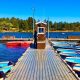 Narrow wooden dock lined with small wooden rental boats on blue lake with trees and sunny skies in background. Lake Cuyamaca, California.