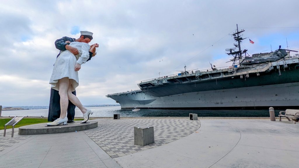 Unconditional Surrender statue of soldier kissing nurse to celebrate end of world war II on the left, USS Midway aircraft carrier on the right