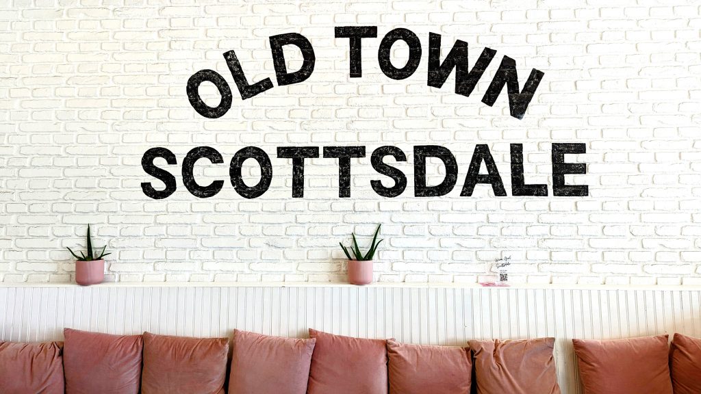 white brick wall with a bench with pink pillows, black writing on the wall: Old Town Scottsdale