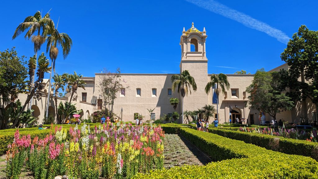 Alcazar Garden Balboa Park with colorful flower beds in the foreground, moorish architecture building with tower in the background 