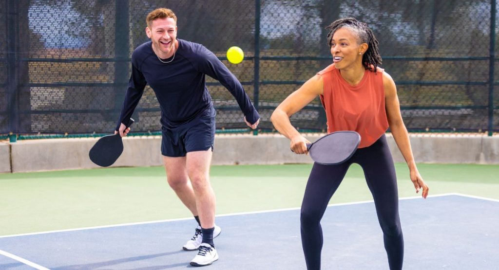 Couple smiling and playing pickleball on outdoor court during summer. Pickleball Courts San Diego.