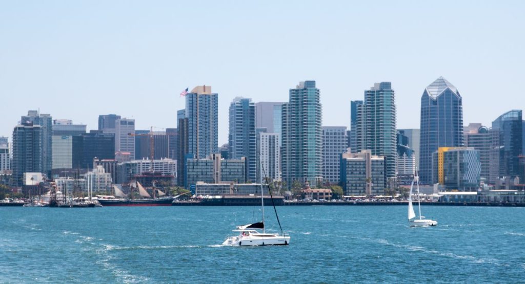 Sail boats on blue water of San Diego Bay with expansive downtown San Diego skyline in background on sunny day. September in San Diego.