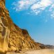 Sandy sea cliffs along white sand beach with Pacific Ocean waves breaking on shore on sunny summer day. Torrey Pines State Reserve, San Diego Blacks Beach, San Diego Nude Beach.
