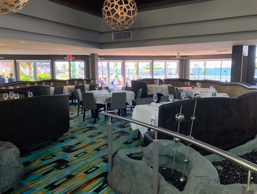 Inside Dining Room at Peohe's Coronado with Blue/Green carpet, Grey furniture, and wall of windows overlooking San Diego Bay