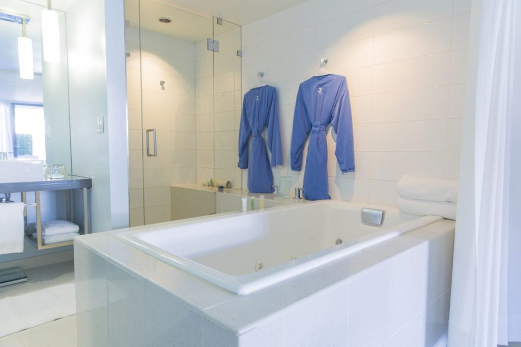 Spacious, white bathroom with large bathtub, glass shower, and two blue robes hanging from wall. Tower 23.
