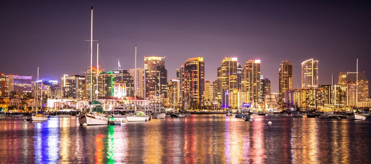 City skyline reflecting on water at night, boats sit on the colorful bay. San Diego skyline at night, Things to do in San Diego in November.