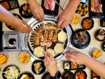 overhead shot over Korean BBQ with hands reaching in and many side dishes on the table