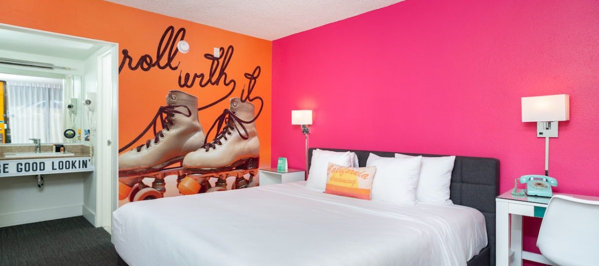Hotel guest room with bright pink wall, and orange accent wall with large mural of roller skates. The Rambler Motel, Sesame Place San Diego Hotels.