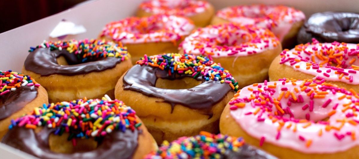 Close up photo of a box of donuts filled with chocolate and pink sprinkled donuts.