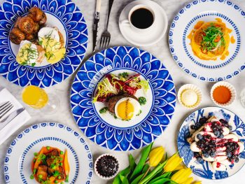Decadent brunch spread on colorful blue plates with yellow tulips, coffee, and mimosas. San Diego Easter Brunch, Herb & Wood.
