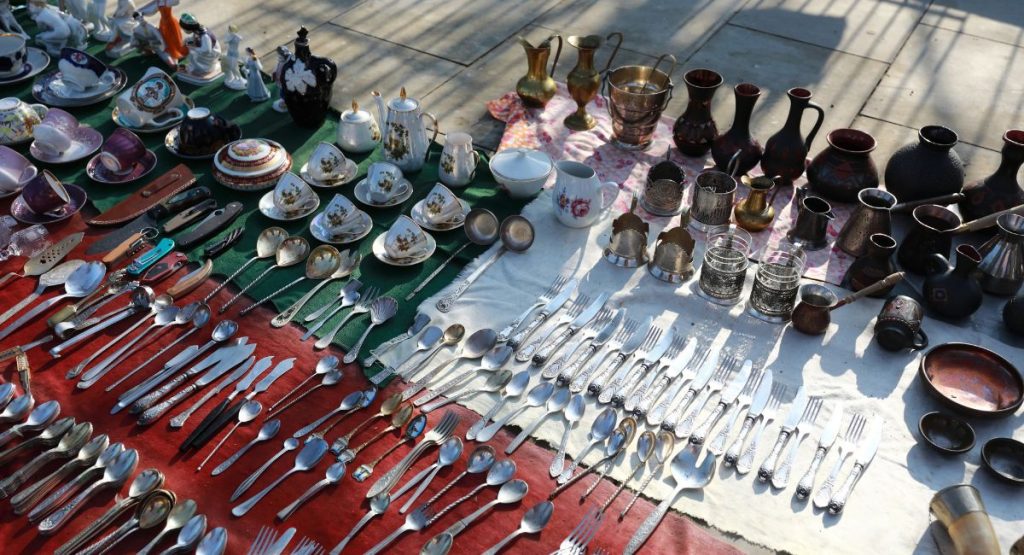 Table full of cutlery, tea cups, and other home goods at swap meet. San Diego Flea Market.